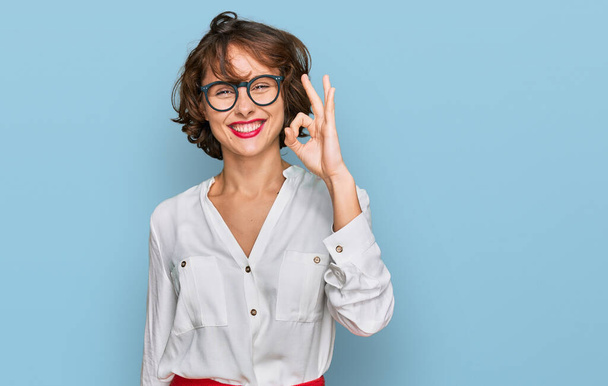 Giovane donna ispanica indossa lo stile di business e occhiali sorridente positivo facendo segno ok con mano e dita. espressione di successo.  - Foto, immagini
