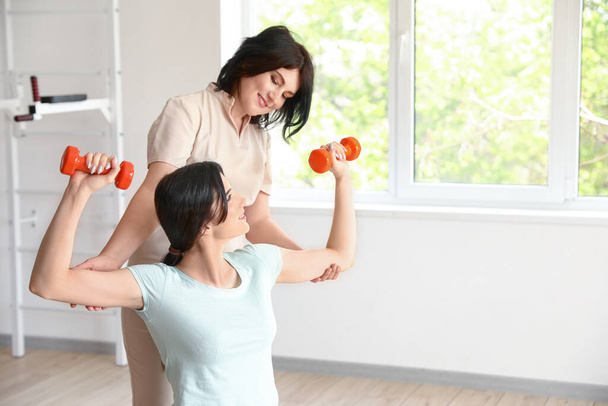 Mujer joven entrenando con pesas y fisioterapeuta en centro de rehabilitación - Foto, Imagen