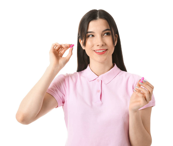 Csinos fiatal nő rózsaszín füldugók fehér háttér - Fotó, kép