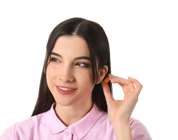 Pretty young woman putting orange ear plug on white background - Photo, Image