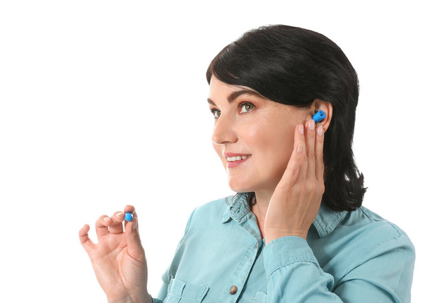 Mujer madura poniendo tapones de oído azul sobre fondo blanco - Foto, Imagen