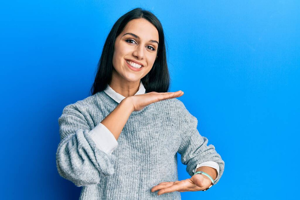 Mujer hispana joven vestida con ropa casual haciendo gestos con las manos mostrando letreros grandes y de gran tamaño, símbolo de medida. sonriendo mirando a la cámara. concepto de medición.  - Foto, imagen