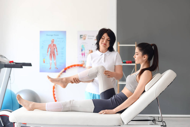 Fisioterapeuta femenina trabajando con una mujer joven en un sofá en un centro de rehabilitación - Foto, imagen