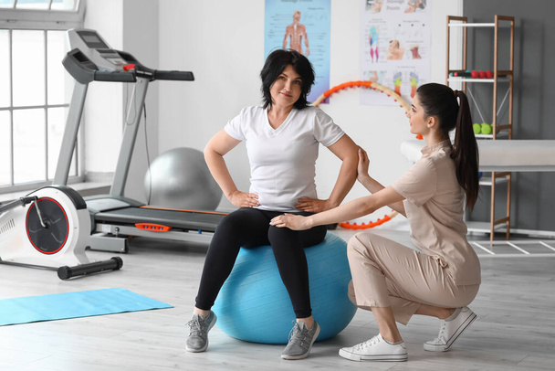Mature woman training with fitball and physiotherapist in rehabilitation center - Фото, изображение