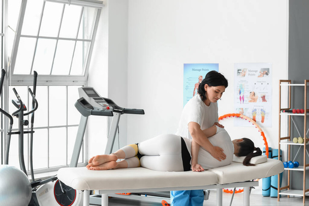 Physiothérapeute mature travaillant avec une jeune femme sur le canapé dans un centre de réadaptation - Photo, image
