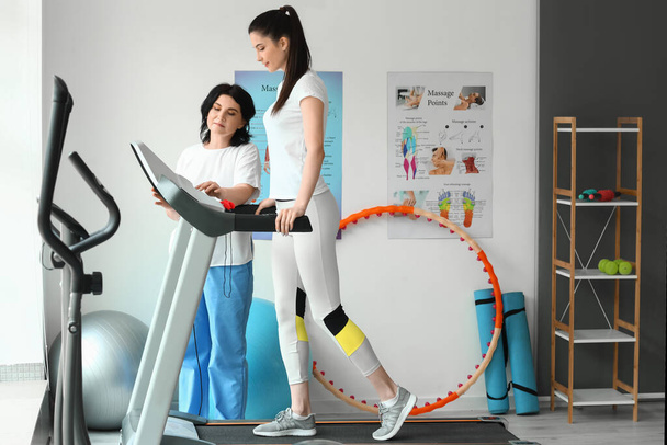 Mature physiotherapist working with young woman on treadmill in rehabilitation center - Photo, Image