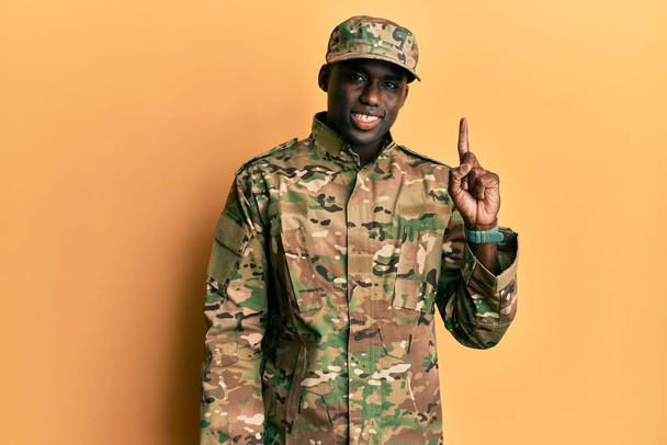 Mladý africký Američan v armádní uniformě ukazující prstem nahoru s úspěšným nápadem. odešel a byl šťastný. číslo jedna.  - Fotografie, Obrázek