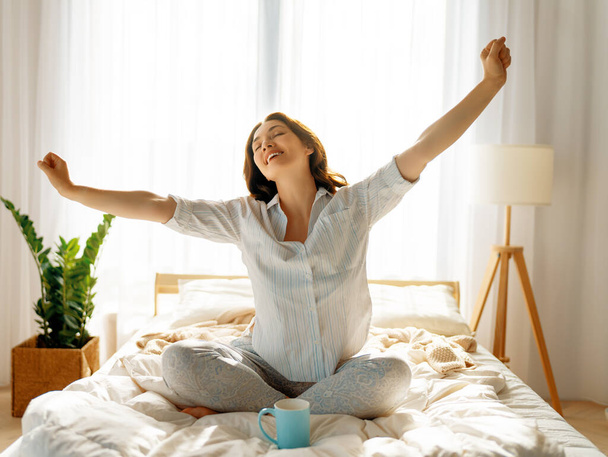 Glückliche junge Frau genießt sonnigen Morgen auf dem Bett.   - Foto, Bild
