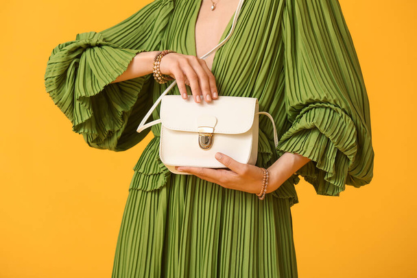 Woman with trendy accessories holding handbag on color background, closeup - 写真・画像