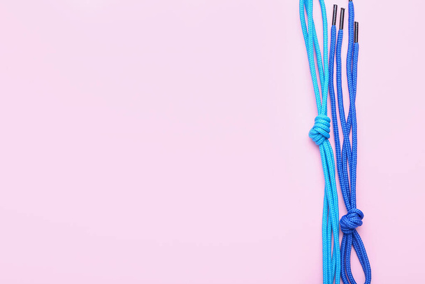 Blue shoe laces tied in knots on pink background, closeup - 写真・画像