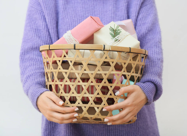 Woman holding basket with Christmas gifts on white background, closeup - Foto, afbeelding