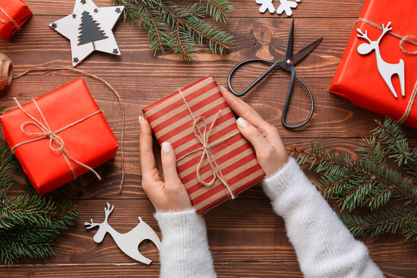 Mains féminines avec cadeaux de Noël, branches de sapin et ciseaux sur fond bois, gros plan - Photo, image