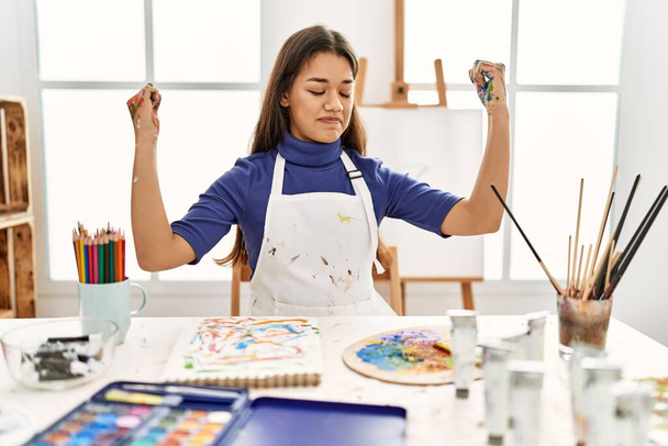 腕の筋肉を示す塗装手でアートスタジオで若いブルネットの女性は誇りに思って笑っています。フィットネスのコンセプト.  - 写真・画像