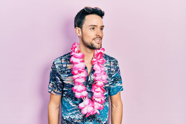 Junger hispanischer Mann trägt Sommer-Stil mit Blick zur Seite, entspannte Profil-Pose mit natürlichem Gesicht und selbstbewusstem Lächeln.  - Foto, Bild