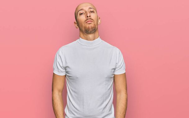 Hombre calvo con barba vistiendo camiseta blanca casual relajado con expresión seria en la cara. simple y natural mirando a la cámara.  - Foto, Imagen