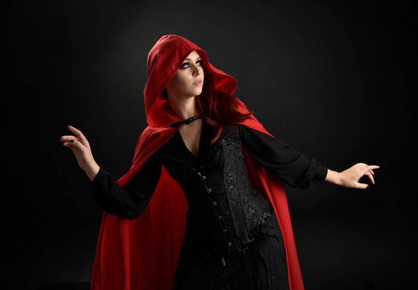 close-up portret van meisje dragen rode manege mantel en heks kostuum, geïsoleerd op zwarte studio achtergrond met schaduwrijke velg verlichting.  - Foto, afbeelding