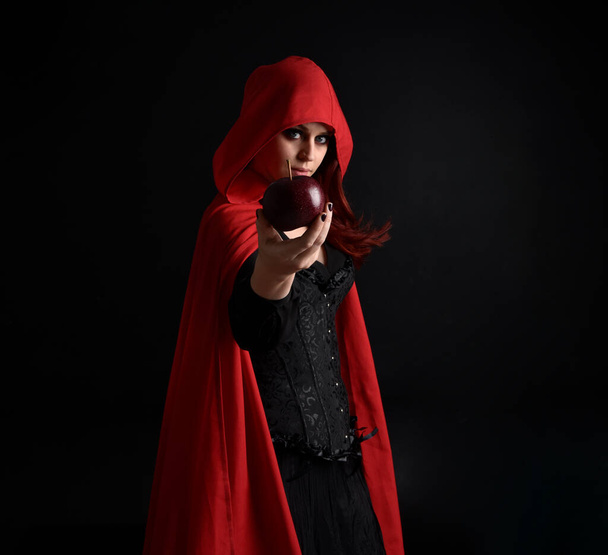 close-up portret van meisje dragen rode manege mantel en heks kostuum, geïsoleerd op zwarte studio achtergrond met schaduwrijke velg verlichting.  - Foto, afbeelding