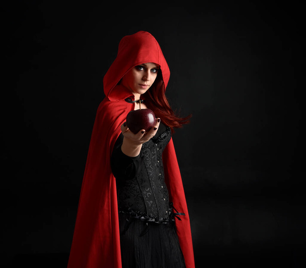 primer plano retrato de niña con capa de capucha roja y traje de bruja, aislado en fondo de estudio negro con iluminación de borde sombreado.  - Foto, imagen