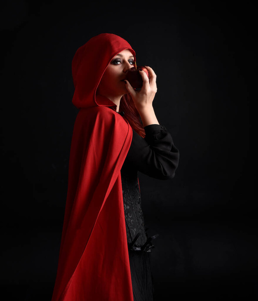 крупним планом портрет дівчини в червоній шапці з капюшоном і костюмом відьми, ізольований на чорному студійному фоні з затіненим фланцем освітлення
.  - Фото, зображення