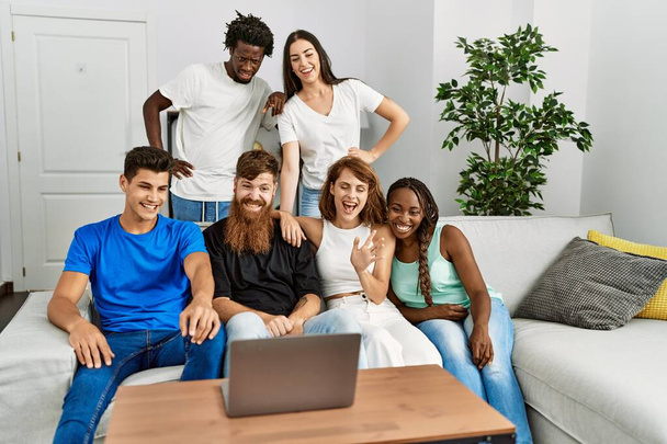 Fiatal barátok csoportja mosolyog boldog birtoklás video hívás segítségével laptop otthon. - Fotó, kép