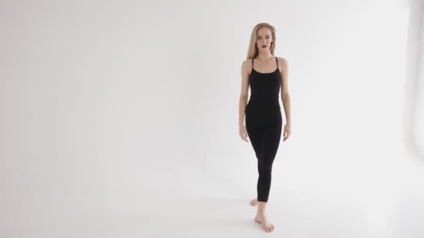 Una joven enérgica con ropa negra estrecha hace una pierna oscilante y toma una división vertical. Concepto de armonía y equilibrio - Metraje, vídeo