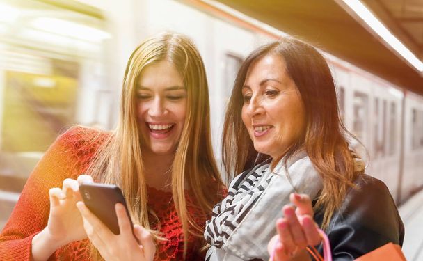 Un par de amigas sonriendo felices mirando al smartphone en una estación de metro
. - Foto, imagen