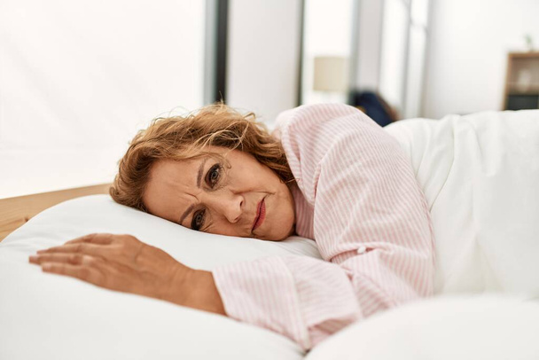 Middle age caucasian woman lying on the bed at bedroom. - Photo, Image