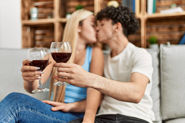 Νεαρό ζευγάρι φιλιά και πρόποση με κόκκινο ποτήρι κρασί στο σπίτι. - Φωτογραφία, εικόνα