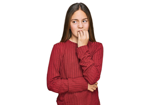 Gyönyörű barna kislány visel alkalmi pulóver néz ki, stresszes és ideges a kezét a száj harapdáló körmök. szorongás.  - Fotó, kép