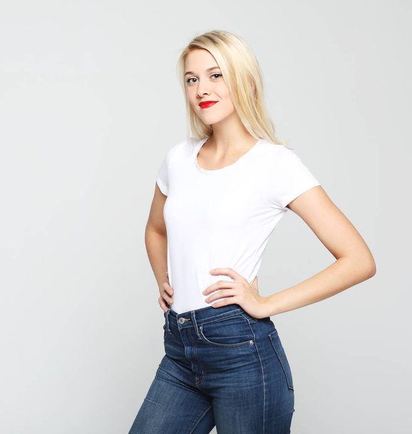 Lifestyle, emotion and people concept: Young cute smiling blond woman wearing white t-shirt over light grey background. - 写真・画像