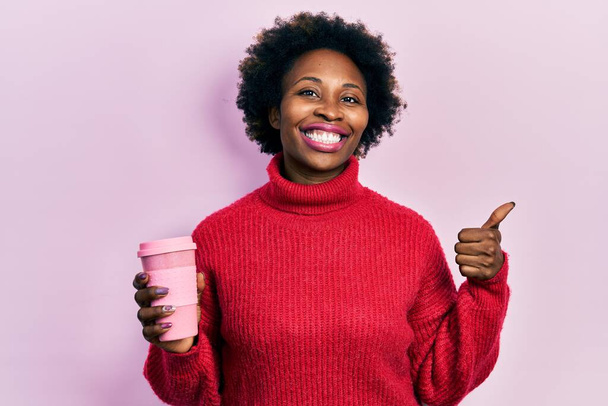 Fiatal afro-amerikai nő iszik egy csésze kávét mosolyogva boldog és pozitív, hüvelykujj fel csinál kiváló és jóváhagyási jel  - Fotó, kép