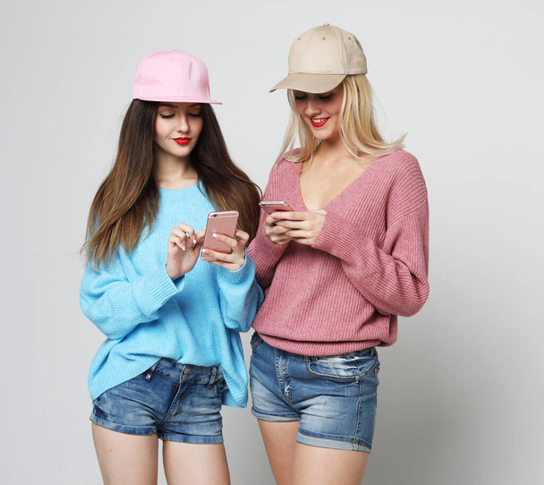Lifestyle, tehnology and people concept: young beautiful women dressed in sweaters and caps are watching news on social networks using smartphones - Foto, afbeelding