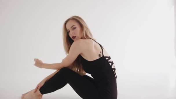 A young girl with a bright make-up in a black top and leggings sits on the floor clasping her knees with her hands. Slow motion - Footage, Video