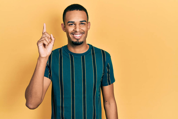 Joven hombre afroamericano con ropa casual apuntando con el dedo hacia arriba con una idea exitosa. exitado y feliz. número uno.  - Foto, imagen