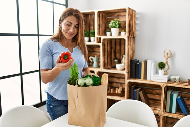Middle age caucasian woman holding paper bag with groceries standing at home. - Photo, Image