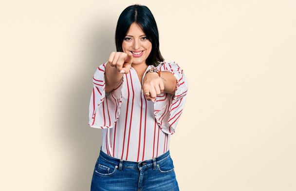 Νεαρή Ισπανίδα που φοράει καθημερινά ρούχα που δείχνουν εσένα και την κάμερα με τα δάχτυλα, χαμογελώντας θετικά και χαρούμενα  - Φωτογραφία, εικόνα