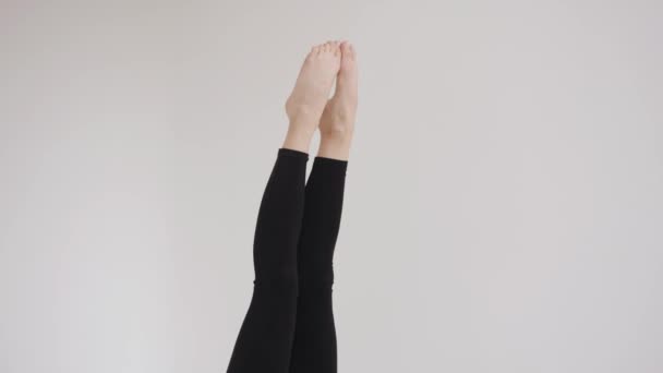 Egy karcsú fiatal lány fekete felsőben és leggings csinál egy nyírfa gyakorlat, és dobja a lábát a feje fölött nyújtás osztályok. Lassú mozgás. - Felvétel, videó