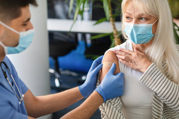 Seniorin wird gegen Covid geimpft, Krankenschwester trägt Klebeverband auf - Foto, Bild