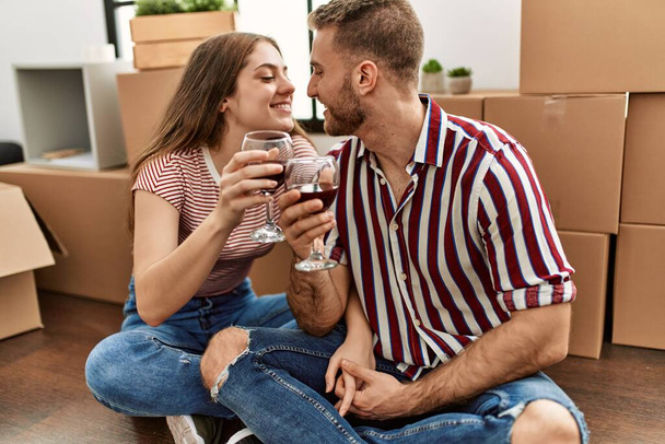 Junges kaukasisches Paar lächelt glücklich und stößt mit Rotwein auf neues Zuhause an - Foto, Bild