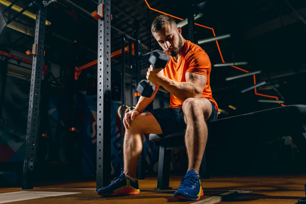 Full-length portrait of young sportive man training, pumping hands with dumbbells in gym - Foto, Bild