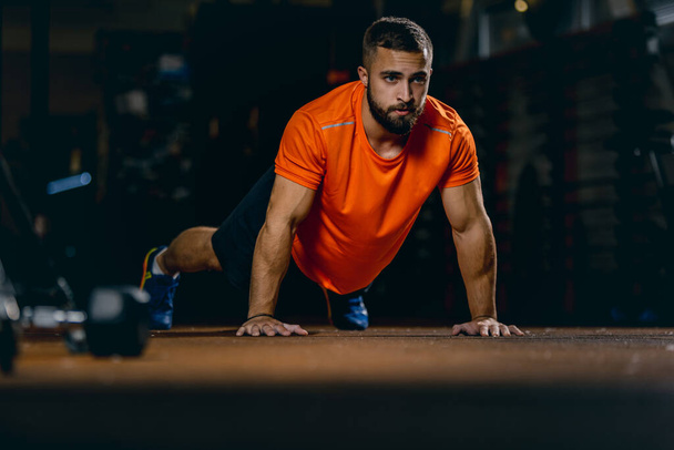 Full-length portrait of sportive man doing push-ups, training in sport gym - Фото, зображення