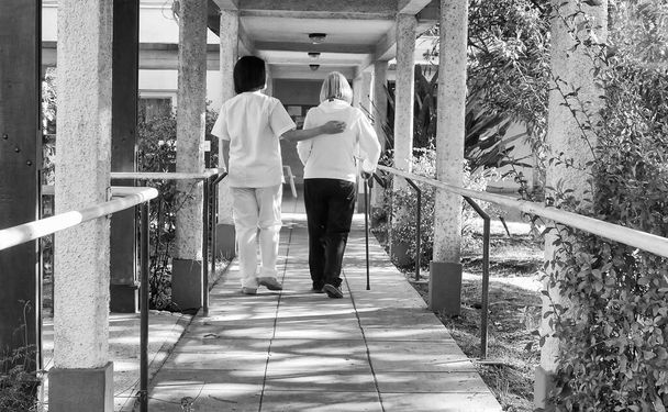 Азіатський лікар допомагає старенькій жінці з палицею ходунків на лікарняному подвір'ї. Реабілітаційна концепція. - Фото, зображення