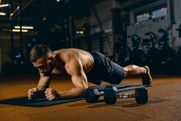 Full-length portrait of young sportive man pumping press, standing in plank position. Gym training - Foto, immagini