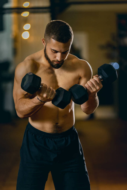 Обрезанный портрет спортивного, концентрированного мужчины, тренирующегося в спортзале, поднимающего гантель - Фото, изображение