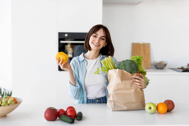 Dieta saludable y estilo de vida. Feliz joven señora desembalaje bolsa de papel con verduras orgánicas frescas, verduras y frutas - Foto, imagen