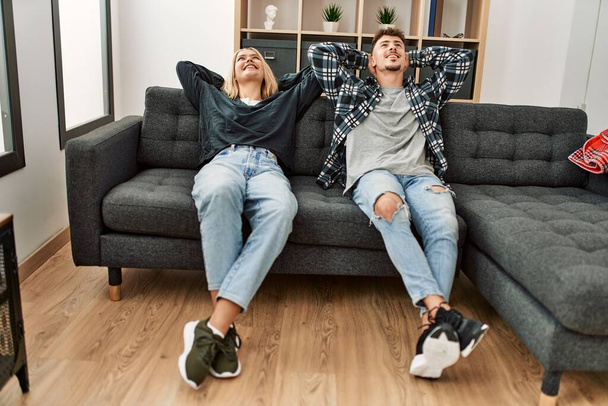 Молода біла пара розслабляється руками на голові, сидячи на дивані вдома
. - Фото, зображення