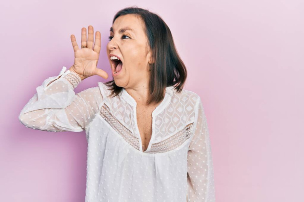 Mujer hispana de mediana edad vistiendo ropa casual gritando y gritando fuerte a un lado con la mano en la boca. concepto de comunicación.  - Foto, Imagen