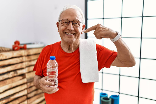 Homme âgé portant des vêtements de sport et serviette à la salle de gym souriant joyeuse montrant et pointant du doigt les dents et la bouche. concept de santé dentaire.  - Photo, image
