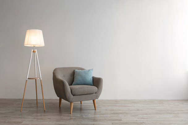 Retro armchair with blue pillow, glowing lamp on floor on gray wall background in office or living room - Valokuva, kuva