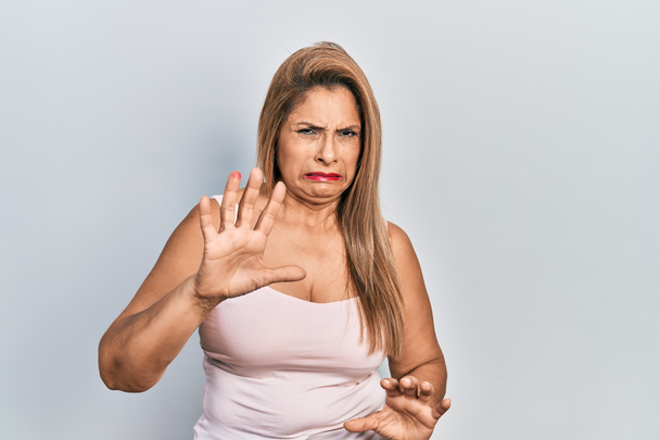 Középkorú spanyol nő visel alkalmi stílus ujjatlan ing undor kifejezés, elégedetlen és félelmetes csinál undor arc, mert ellenszenv reakció. felemelt kézzel  - Fotó, kép